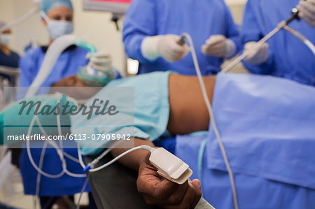 Doctors performing laparoscopic surgery, patient with pulse oxymeter on finger