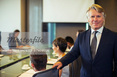Portrait of businessman standing in conference room with colleagues in background
