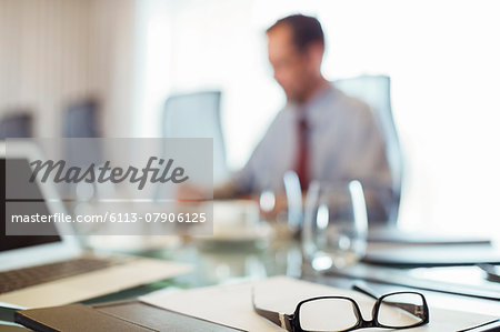 Glasses on conference table, businessman sitting in background