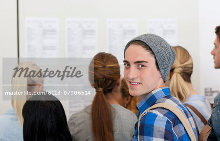 Male student smiling at camera while others read notice board