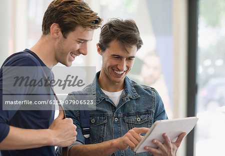 Two male students looking at digital tablet and laughing