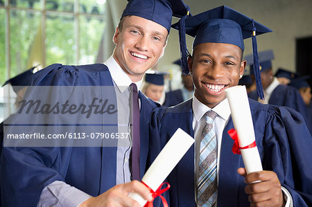 Two laughing male students in graduation clothes holding diplomas