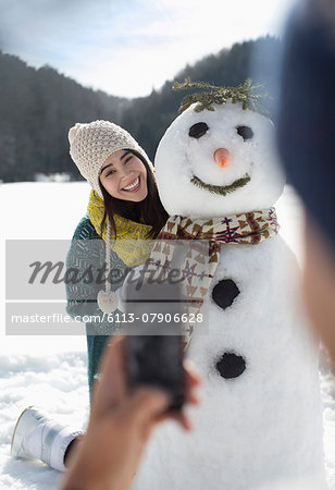 Man photographing woman with snowman