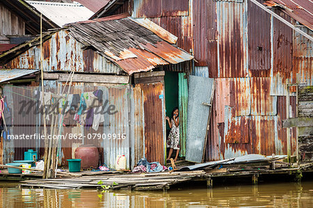 Indonesia, South Kalimatan, Banjarmasin. A house on the Barito River with a young girl sucking a lollipop.