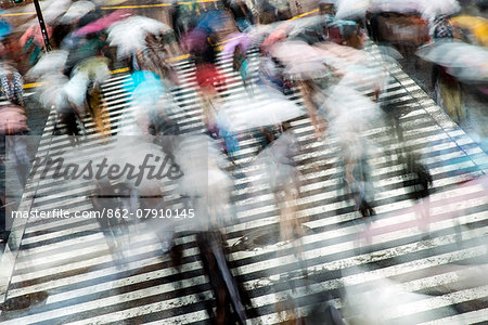 Blurred pedestrians with umbrellas crossing the street at Shibuya crossing, Tokyo, Japan