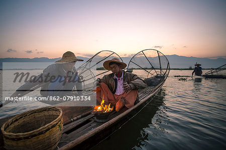 Myanmar, Shan state,  Nyaungshwe Township. Local Intha fishermen warming up on their boat before fishing (MR)