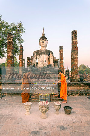 Thailand, Sukhothai Historical Park. Two buddhist monks offering flowers at Wat Mahathat temple at sunrise (MR)