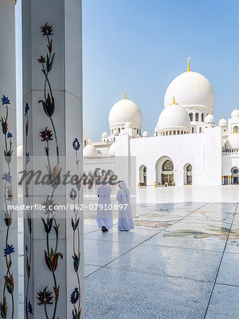 United Arab Emirates, Abu Dhabi. Two arabic men in traditional dress walking inside Sheikh Zayed Grand Mosque