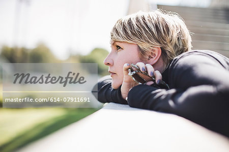 Mature woman gazing from footbridge wall holding onto smartphone Mature woman gazing from footbridge wall holding onto smartphone
