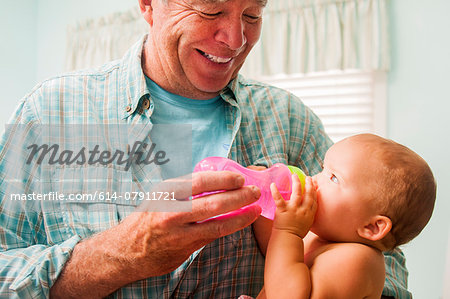 Grandfather bottle feeding baby granddaughter on lap in living room