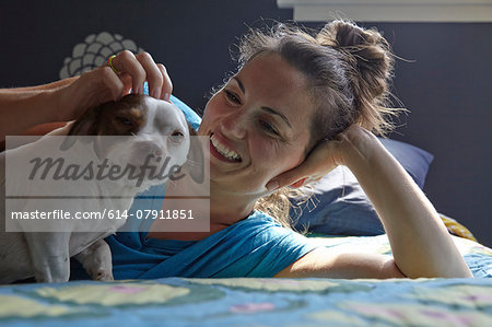 Woman lying on bed petting dog