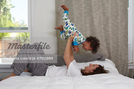 Young woman lying on bed lifting up toddler son