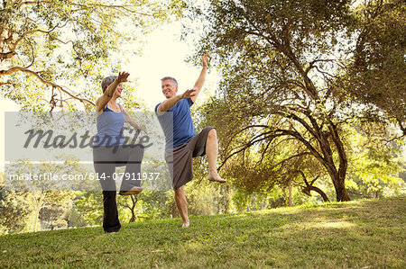 Mature couple practicing yoga positions in park