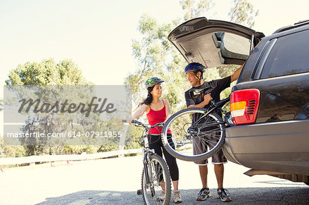 Mature couple removing bicycles from car boot in park Mature couple removing bicycles from car boot in park