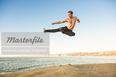 Mid adult man on beach, mid air in kung fu jump