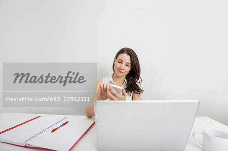 Young businesswoman using cell phone at desk in office