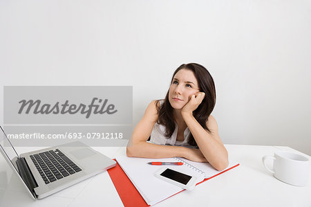 Thoughtful businesswoman with laptop and binder at desk in office