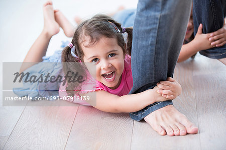Portrait of playful girl with sister holding father's legs on hardwood floor