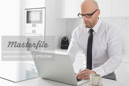 Mid adult businessman using laptop at kitchen counter