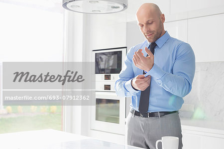 Mid adult businessman buttoning sleeve at home