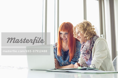 Smiling businesswomen using laptop together in creative office