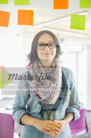 Portrait of smiling businesswoman standing by glass wall with sticky notes in office