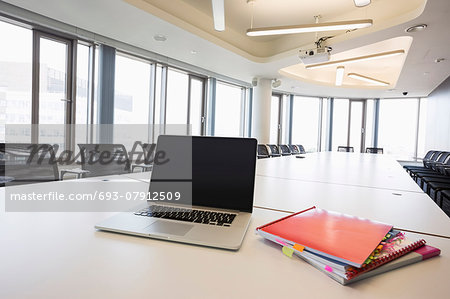 Laptop and files on empty conference table in creative office