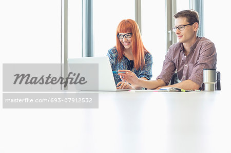 Business colleagues using laptop at desk in creative office