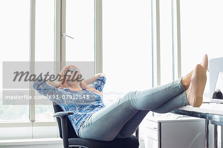 Full-length of businesswoman relaxing with feet up at desk in creative office
