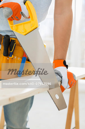 Midsection of man sawing wood in new house