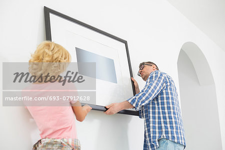 Couple hanging picture frame on wall in new house