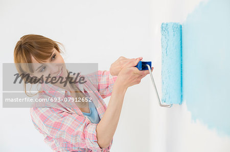 Beautiful woman painting wall with paint roller