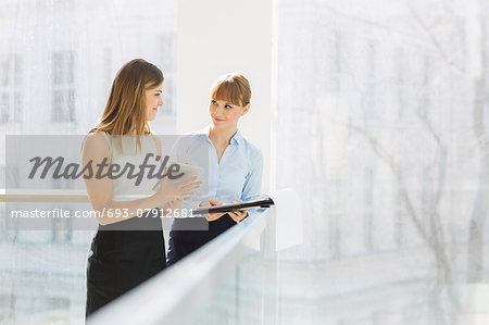 Businesswomen discussing over tablet PC while standing by railing in office