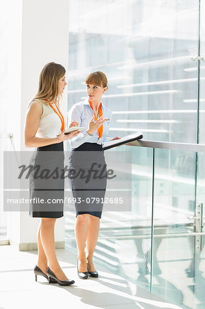 Full-length of businesswomen discussing over tablet PC while standing by railing in office