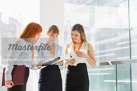 Businesswomen doing paperwork by railing in office