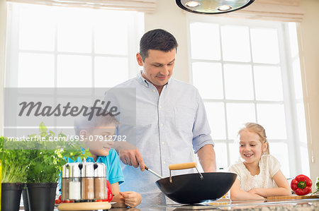 Children looking at father preparing food in kitchen