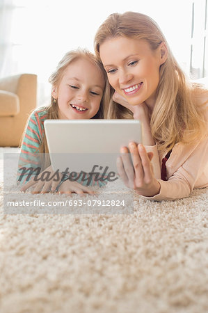 Happy mother and daughter using digital tablet on floor at home