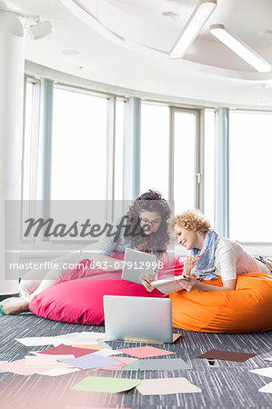 Businesswomen using tablet PC while relaxing on beanbag chairs at creative office