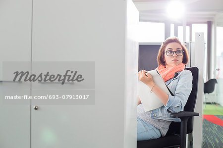 Businesswoman holding notepad while sitting on chair at creative office