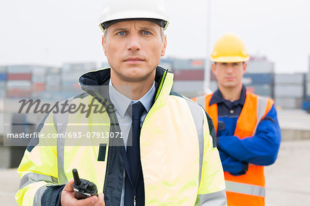 Portrait of confident worker standing with coworker in background at shipping yard