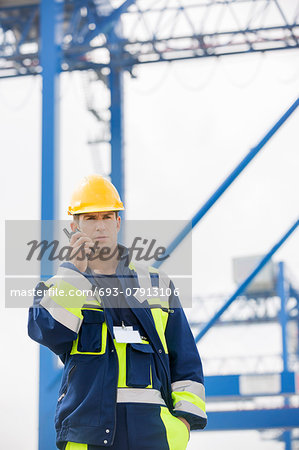 Mid adult male worker using walkie-talkie in shipping yard