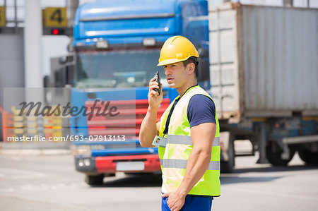 Mid adult man using walkie-talkie in shipping yard