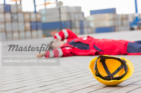 Yellow hardhat at shipyard with depressed male worker lying in shipping yard