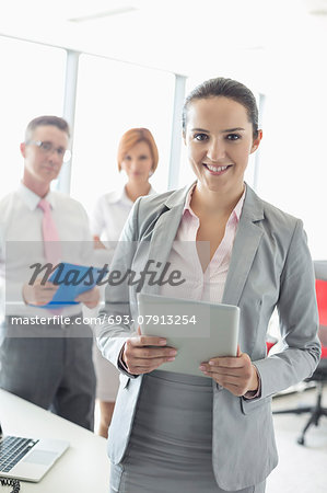 Portrait of happy businesswoman holding digital tablet with colleagues in background at office