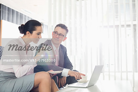 Businessman and businesswoman discussing over laptop in office