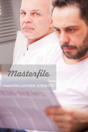 serious man with a friend reading newspaper in a living room