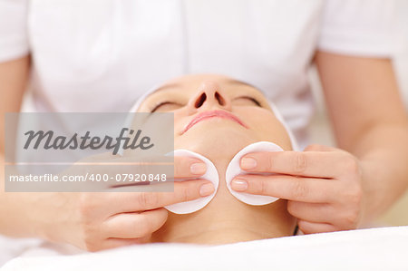 Close-up shot of a womans face being cleaned with cotton discs by a cosmetician