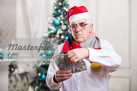 Senior man in Santa's hat holding money over Christmas background