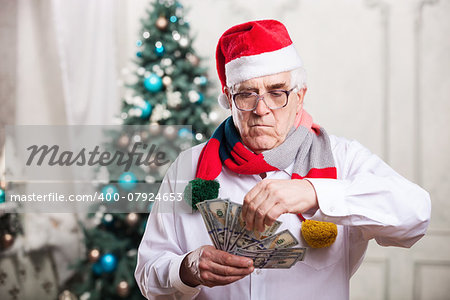 Senior man in Santa's hat holding money on Christmas background