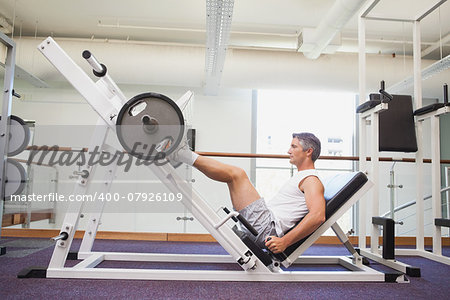 Fit man lifting heavy barbell with legs at the gym